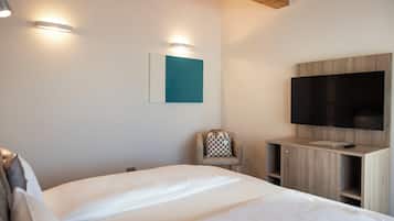 A modern hotel room with a large bed, a flat-screen TV mounted on a wooden cabinet, and a chair with a checkered cushion.