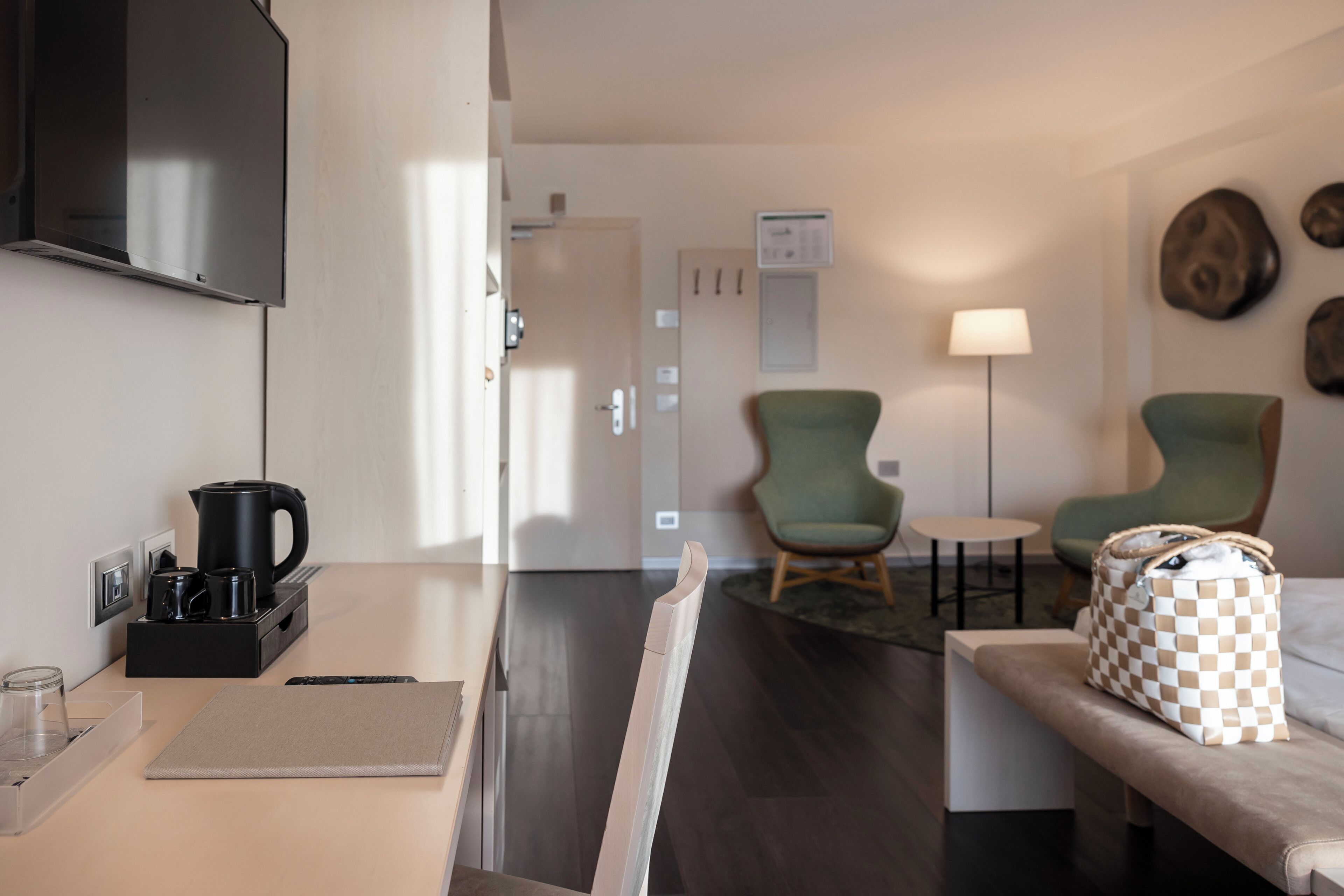 Una habitación de hotel moderna con kitchenette, un área de descanso con dos sillones, un sofá y un bolso cuadriculado sobre el sofá.