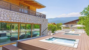 A wooden deck with a pool, lounge chairs, and a stone wall. - Blu Hotel Natura & Spa - Adults Only (Folgaria)