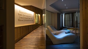 A modern spa area with a wooden floor, a relaxation lounge, and a wall with multilingual water-related text. - Blu Hotel Natura & Spa - Adults Only (Folgaria)