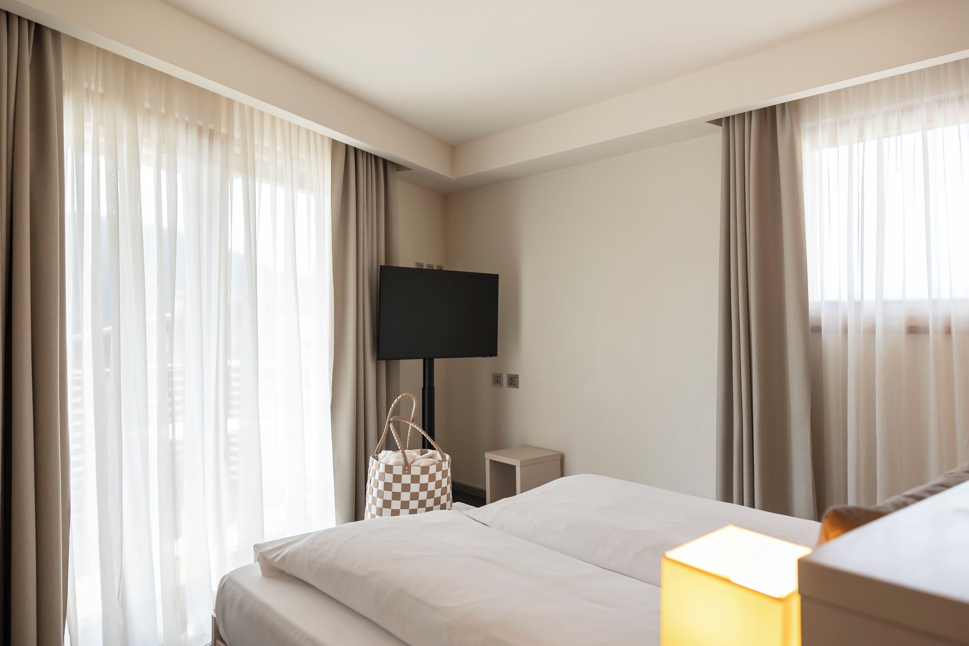 A hotel room with a bed, a TV, a bedside table, a lamp, and a checkered bag.