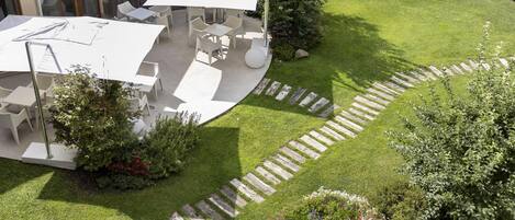 Un patio trasero con área de terraza, mobiliario exterior y un jardín con un sendero de madera.