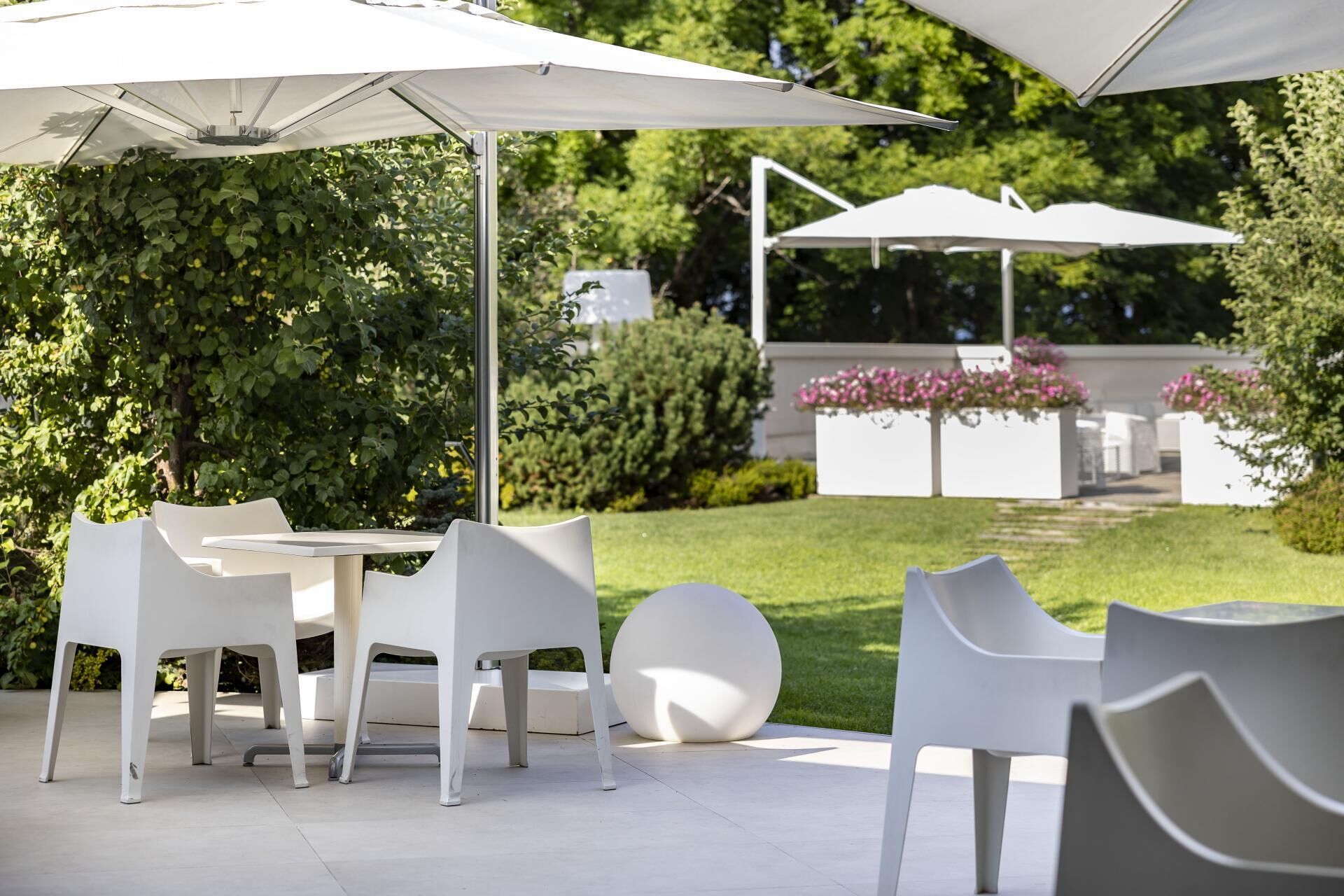 Un espace extérieur aménagé en terrasse, avec des tables et des chaises blanches, entouré de verdure et agrémenté de parasols.