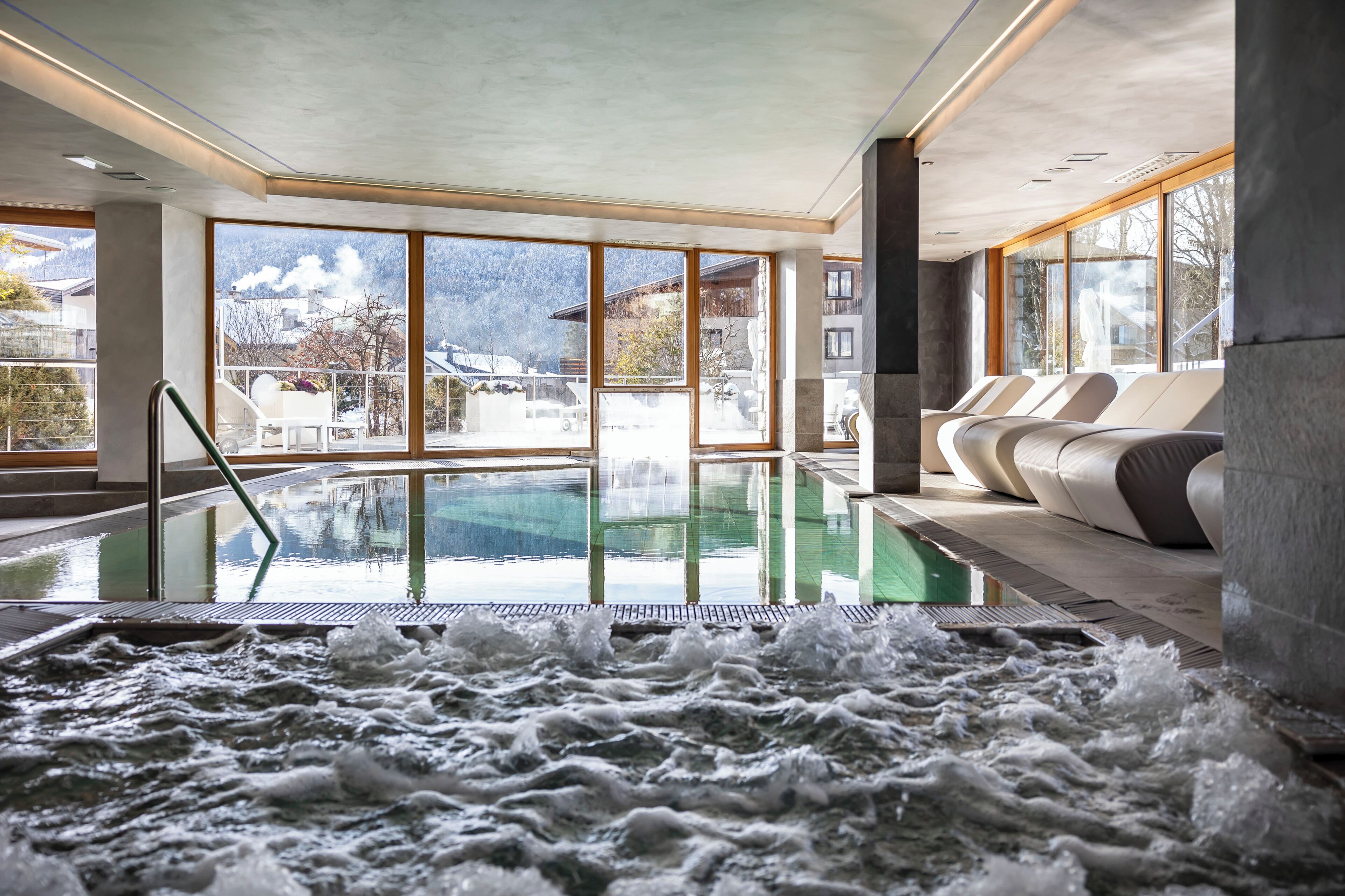 Un área de spa con un jacuzzi, asientos y vistas a un paisaje montañoso nevado.