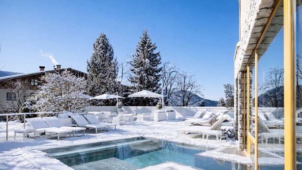 A snow-covered outdoor pool area with lounge chairs and umbrellas, surrounded by trees and buildings. - Blu Hotel Natura & Spa - Adults Only (Folgaria)