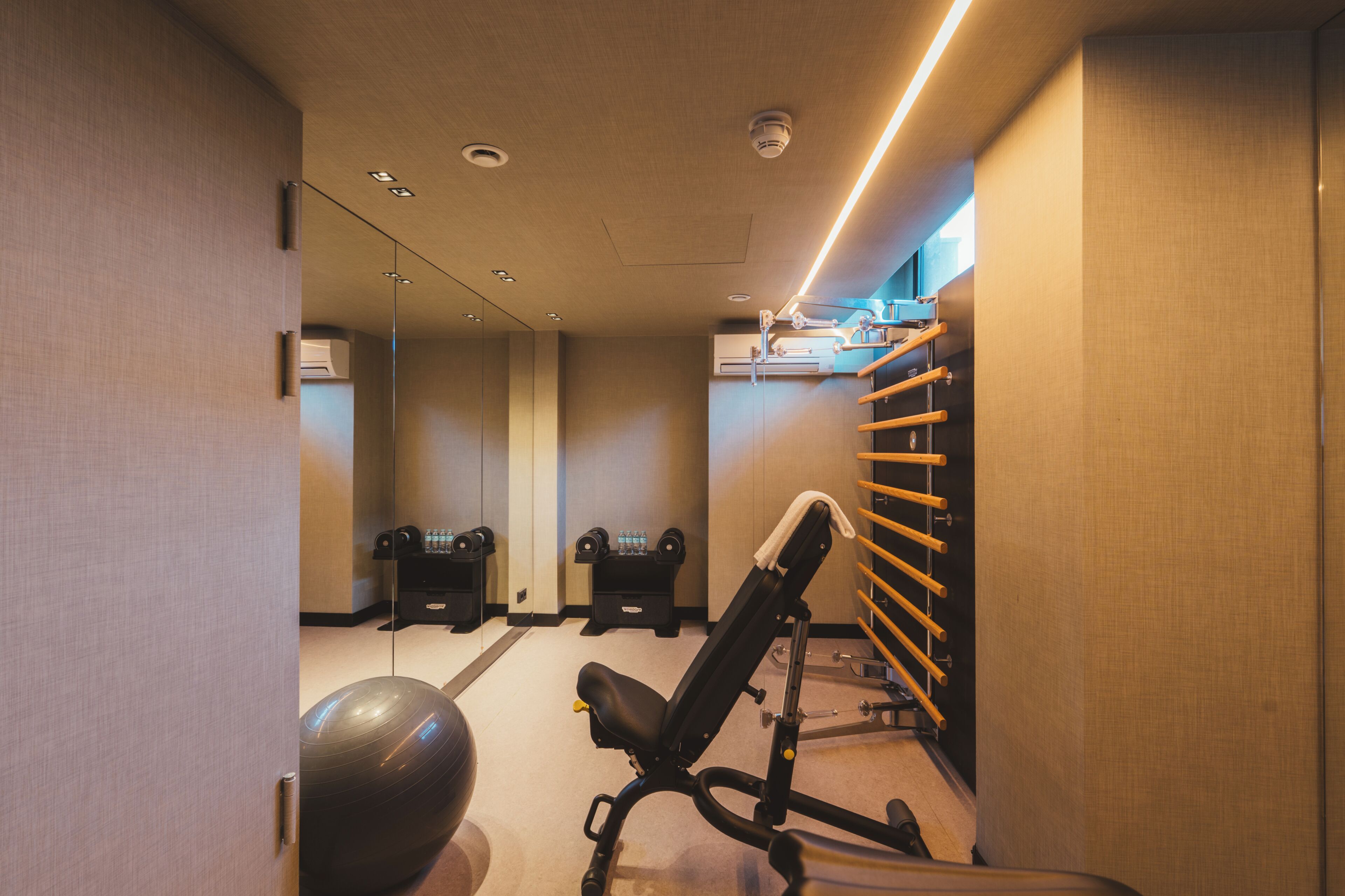 Un gimnasio con equipo de ejercicio, un espejo en la pared y iluminación empotrada en el techo.