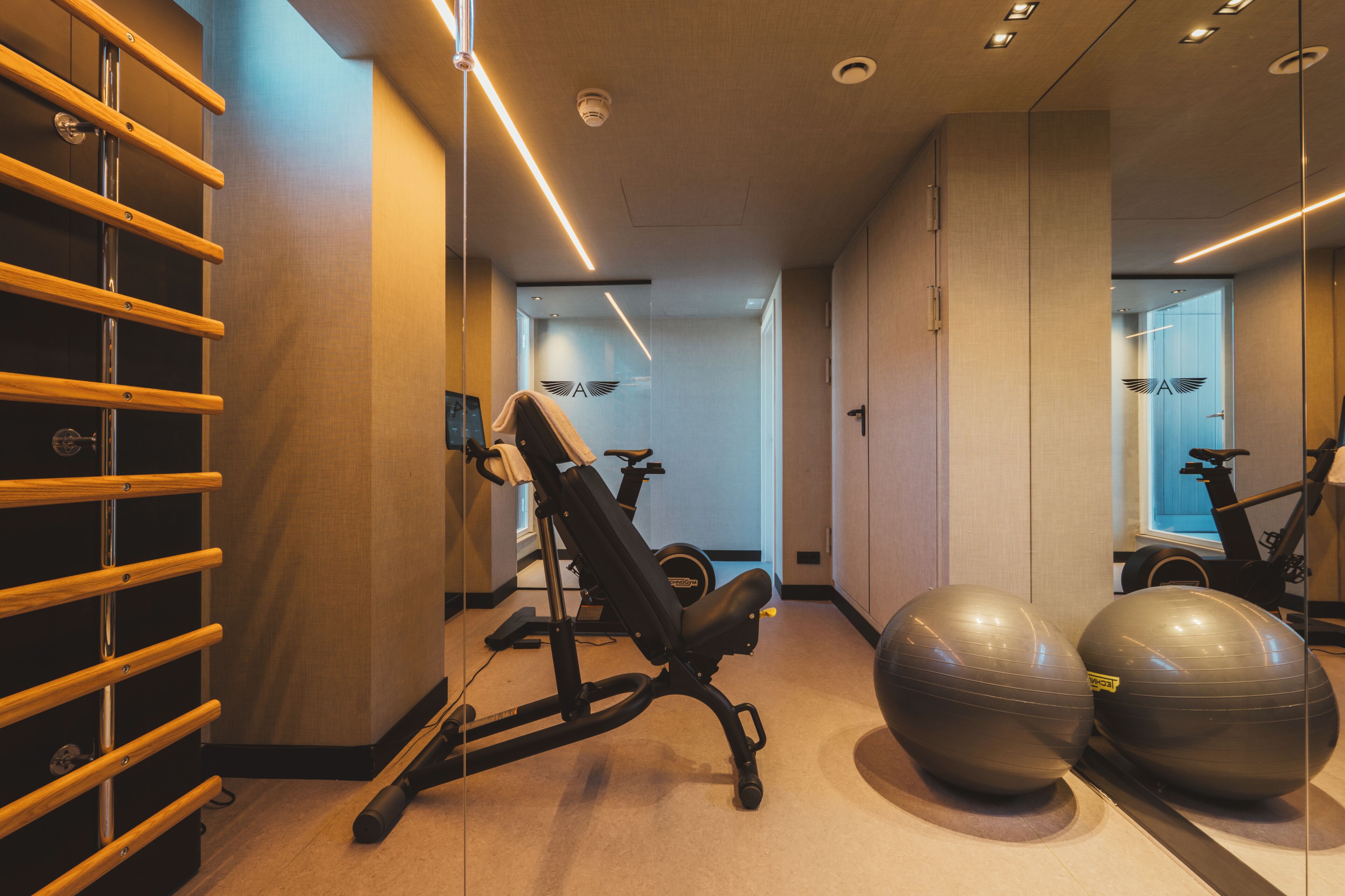 Ein Fitnessraum mit Trainingsgeräten, einem an der Wand befestigten Rack und einem Spiegel, der den Raum reflektiert.