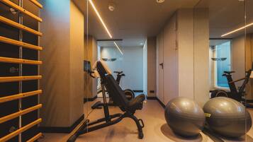 Ein Fitnessraum mit Trainingsgeräten, einem an der Wand befestigten Rack und einem Spiegel, der den Raum reflektiert.