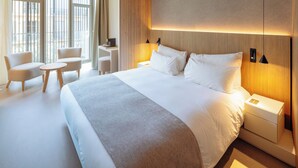 Moderni hotellihuone, jossa on suuri sänky, kaksi yöpöytää, työpöytä ja kaksi tuolia.