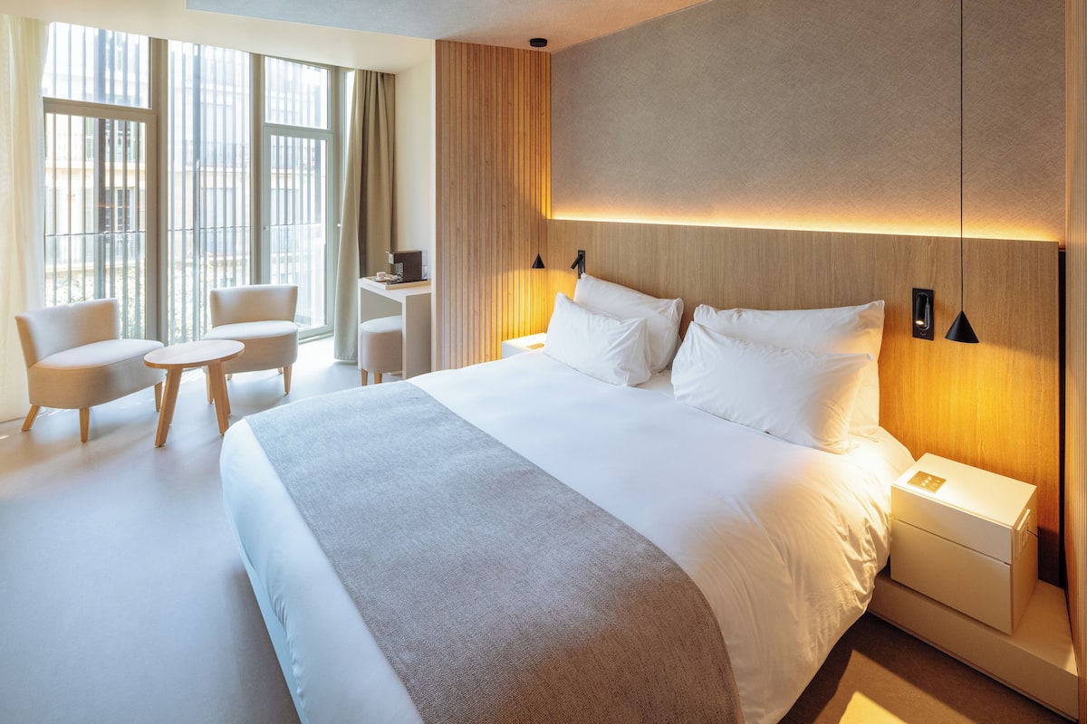 Moderni hotellihuone, jossa on suuri sänky, yöpöydät, työpöytä ja kaksi tuolia.