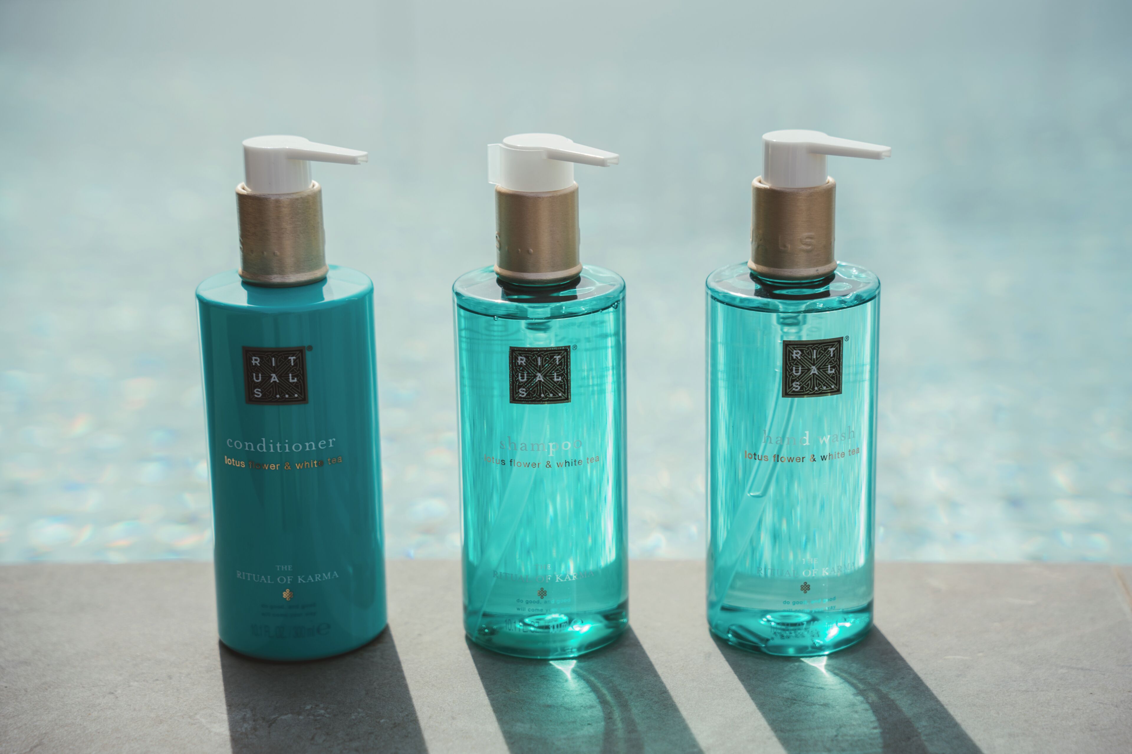 Three bottles of RITUALS conditioner by The Ritual of Karma on a reflective surface.