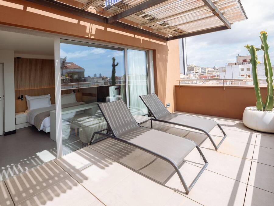A modern hotel room with a balcony, a bed, a desk, and a potted cactus.