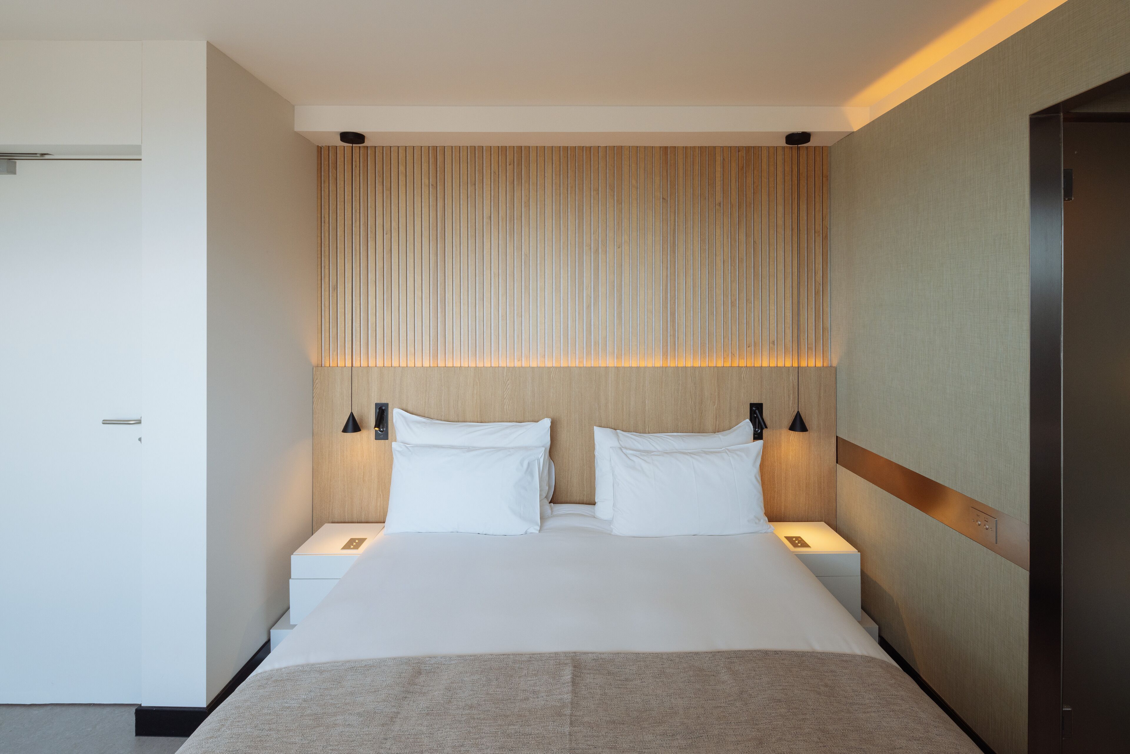 A modern hotel room with a large bed, two bedside tables, and a headboard with vertical lines.