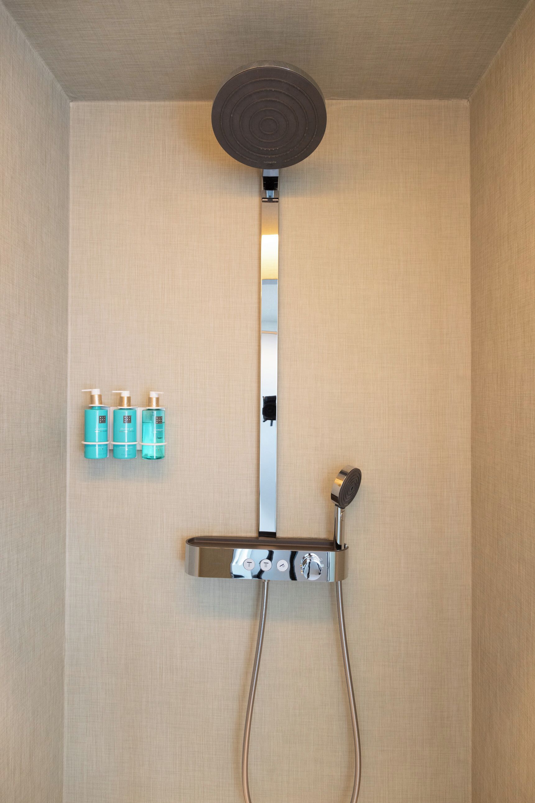Een moderne douche met een bedieningspaneel en drie shampoo flessen aan de muur.