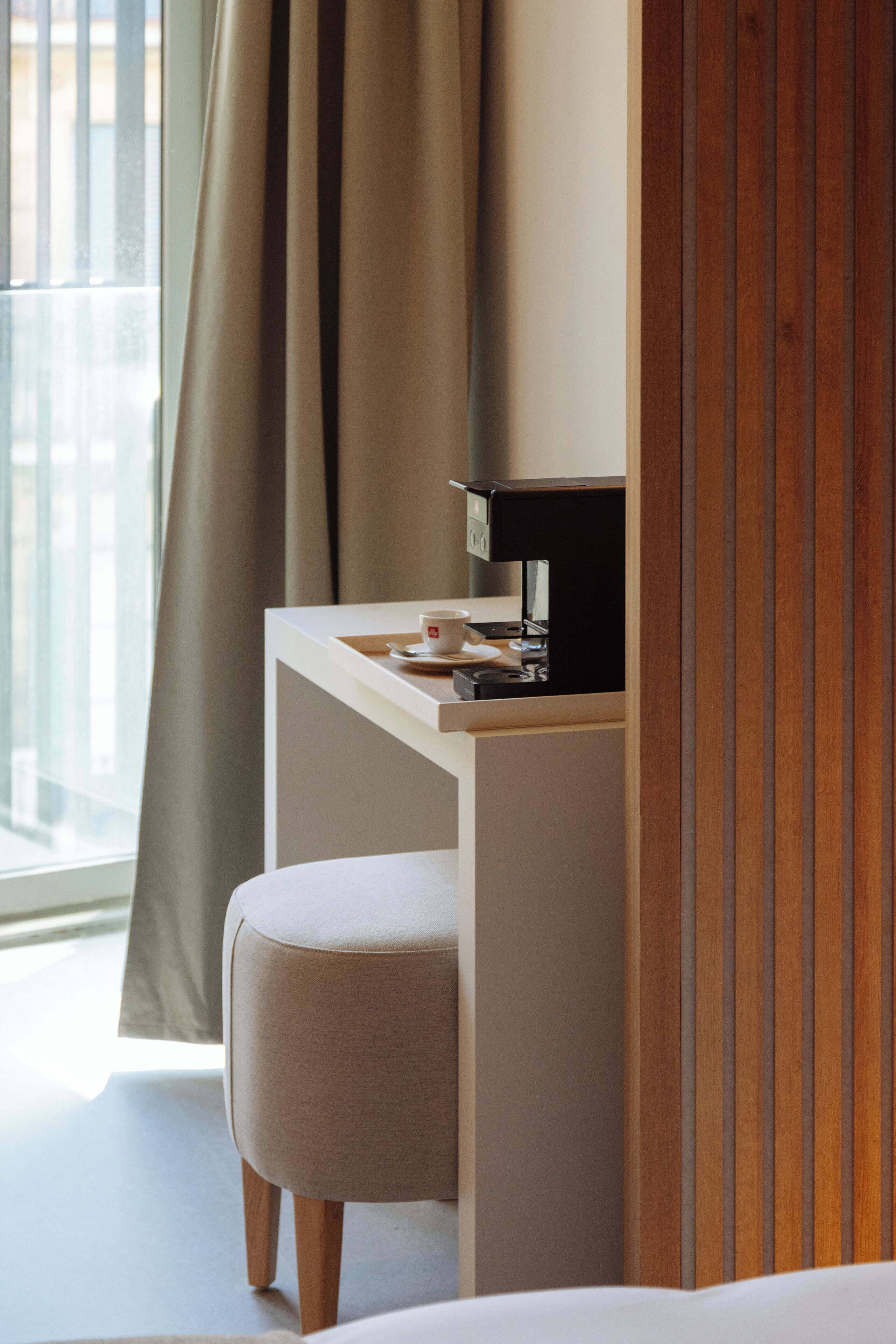 Een hotelkamer met een bed, een bureau met een lamp, een koffieapparaat en een raam met gordijnen.