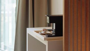 Een hotelkamer met een bed, een bureau met een lamp, een koffieapparaat en een raam met gordijnen.