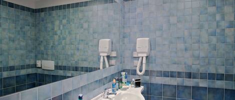 Baño con azulejos azules, un lavamanos, un espejo y dos secamanos.