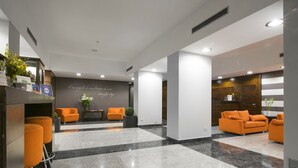 Un hall d’entrée moderne avec un comptoir d’accueil, deux espaces de détente dotés de fauteuils orange et un sol en marbre.