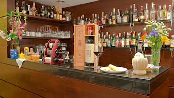 Un espace bar avec des étagères remplies de bouteilles d’alcool, une bouteille de vin, une caisse enregistreuse et un vase avec des fleurs.