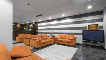 Un salon moderne avec des canapés orange, un téléviseur à écran plat et un mur à rayures.