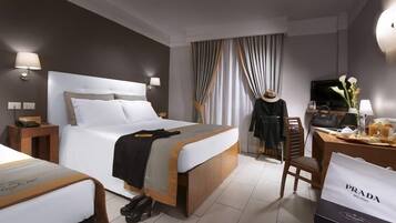 A hotel room with a large bed, bedside tables, a desk with a chair, a TV, and a Prada shopping bag.
