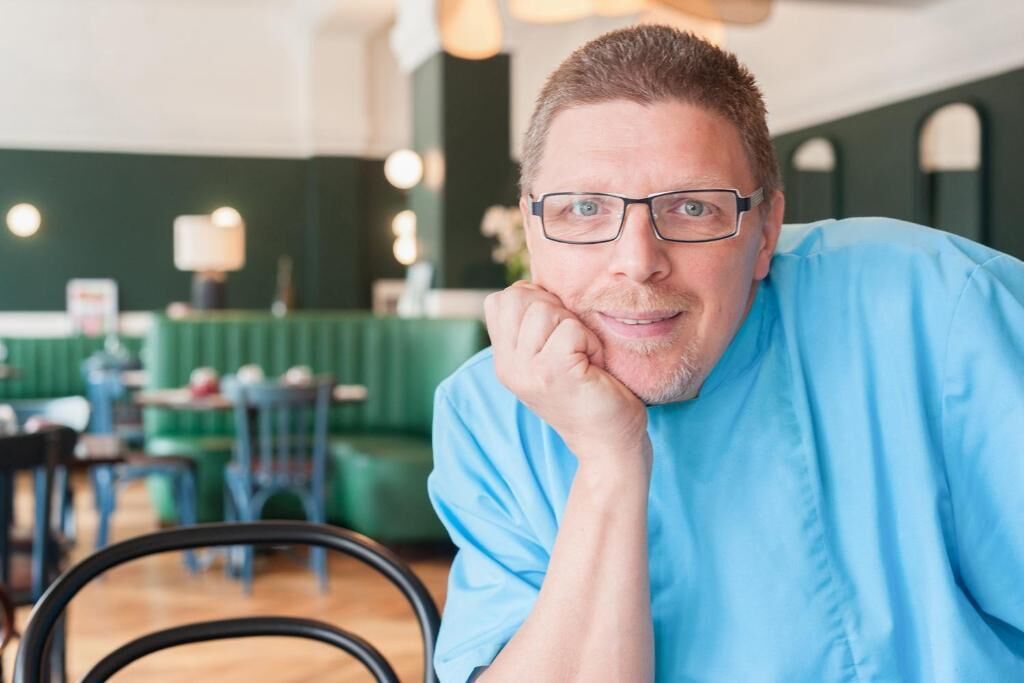 Una persona sentada en un restaurante con un asiento tapizado en verde y una mesa de madera.