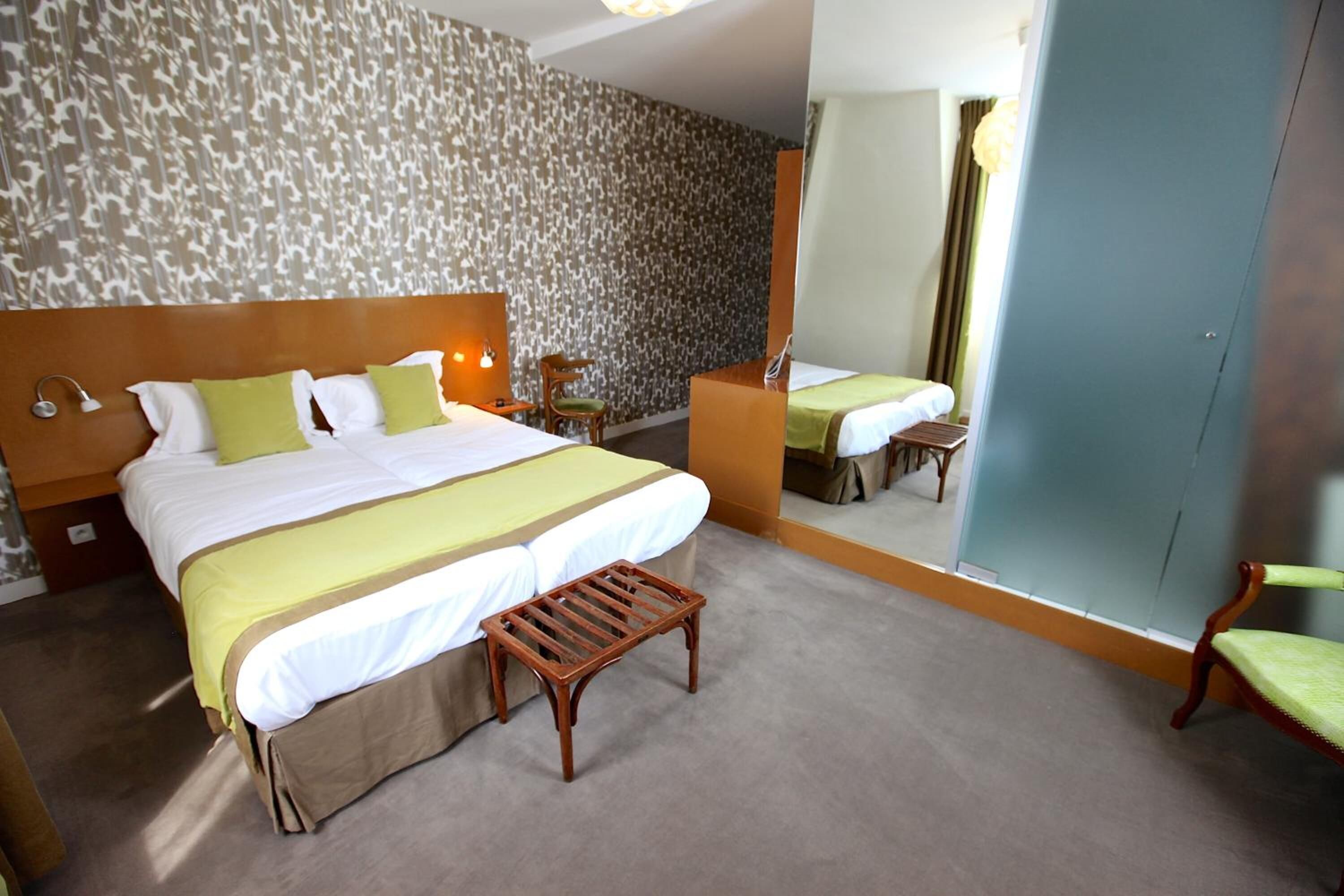 A hotel room with a large bed, a wooden bench, a desk, and a chair.