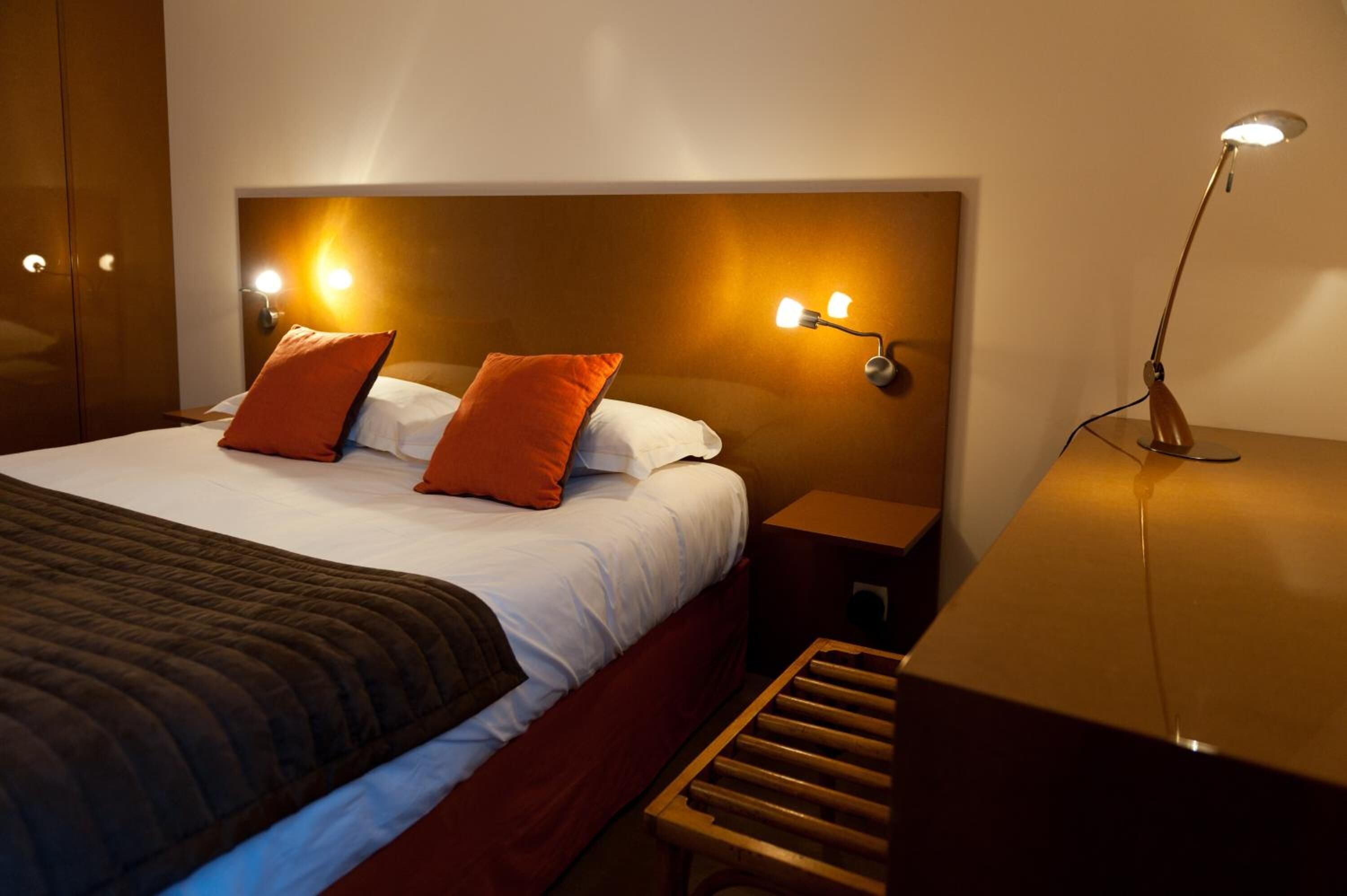 Una habitación de hotel con una cama grande, dos mesitas de noche, un tocador y un banco de madera.
