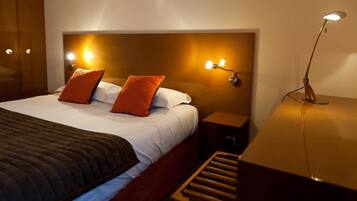 A hotel room with a large bed, two bedside tables, a nightstand, and a wooden bench.