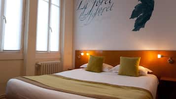 A neatly made bed with a green throw blanket, a headboard with wall-mounted lights, and a window with blinds.