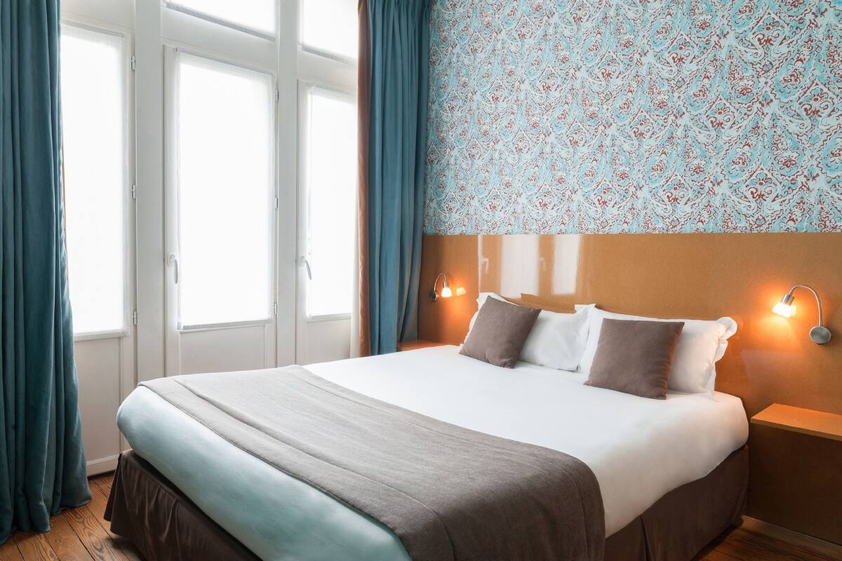A hotel room with a large bed, a nightstand with a lamp, and a patterned wall.