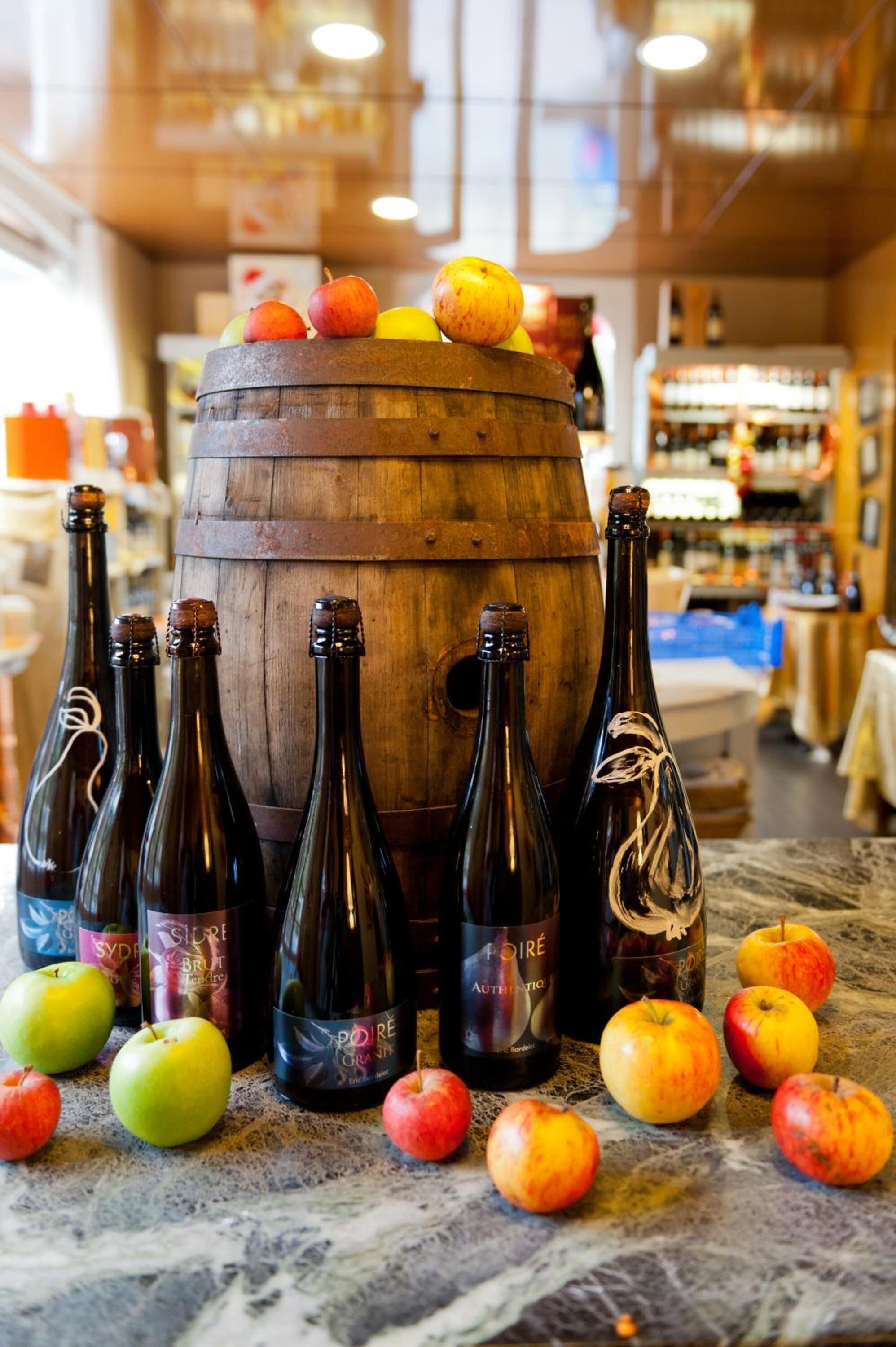 Un barril de madera rodeado de botellas y manzanas sobre una superficie de mármol.