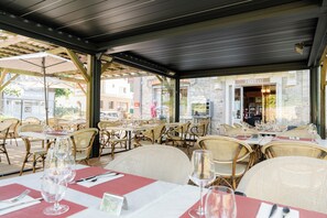 An outdoor dining area with wicker chairs and tables, some with wine glasses and menus. - The Originals Boutique, H ôtel Ô Gayot (Bagnoles-de-l'Orne)
