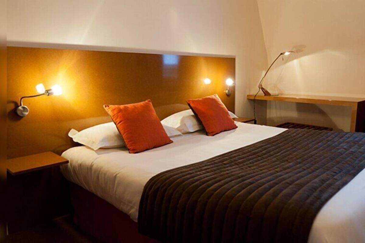 A hotel room with a bed, nightstands, a desk, and a chair.