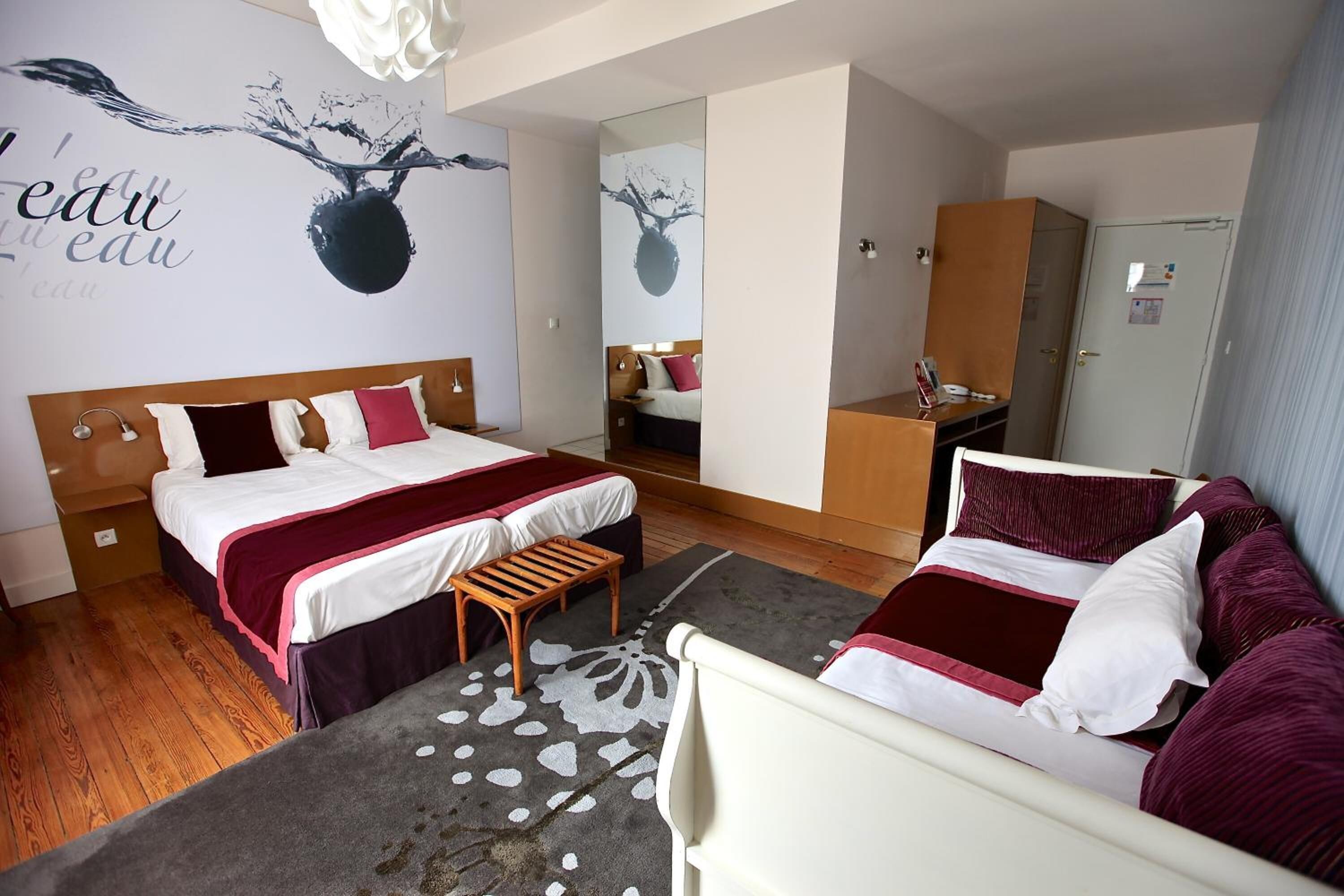 Una camera d'albergo con un letto grande, un letto più piccolo, una scrivania e un armadio.