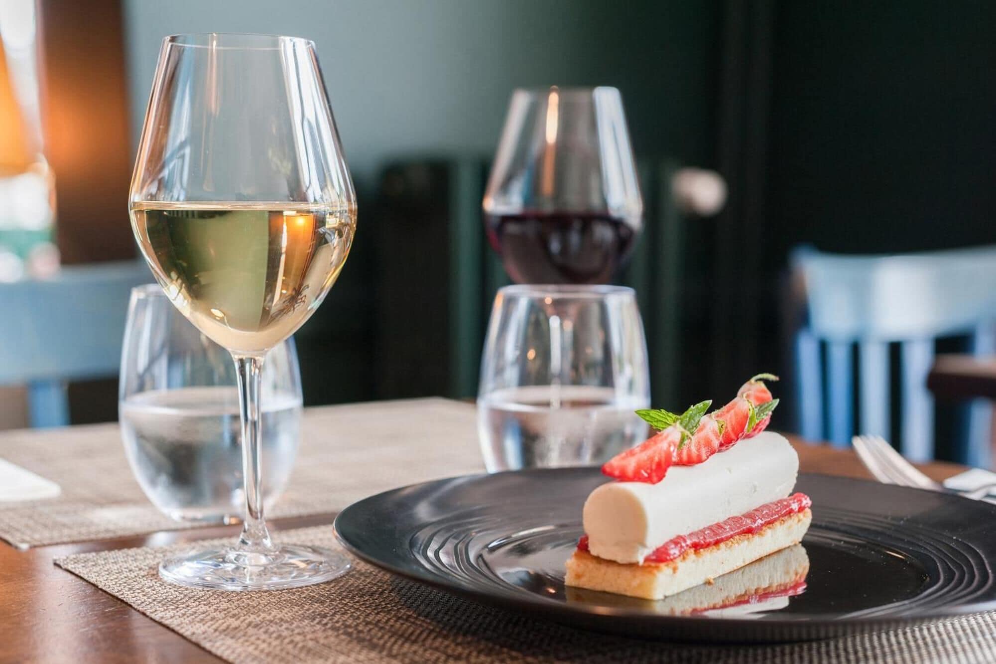 Een dessert op een zwart bord, met een glas witte wijn en een glas rode wijn op de achtergrond.