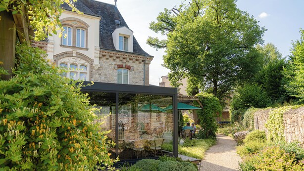 Ein Gartenweg führt zu einem Gebäude mit einer Glaskuppel und Sitzgelegenheiten im Freien.