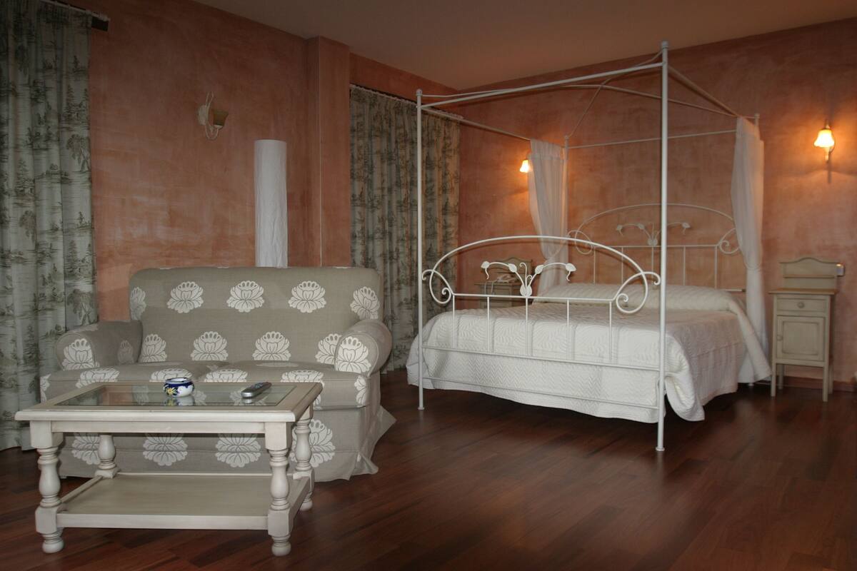 A bedroom with a four-poster bed, a sofa, a nightstand, and a glass-top coffee table.