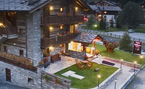 Un hôtel aménagé dans un chalet en rondins, doté d’une façade en pierre, d’un espace extérieur avec des sièges et d’une enseigne indiquant « Hôtel Bellevue ».