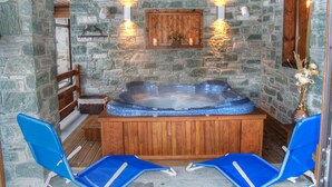 A stone-walled room with a hot tub, wooden ceiling, and two blue chairs. - Bellevue (Ayas)