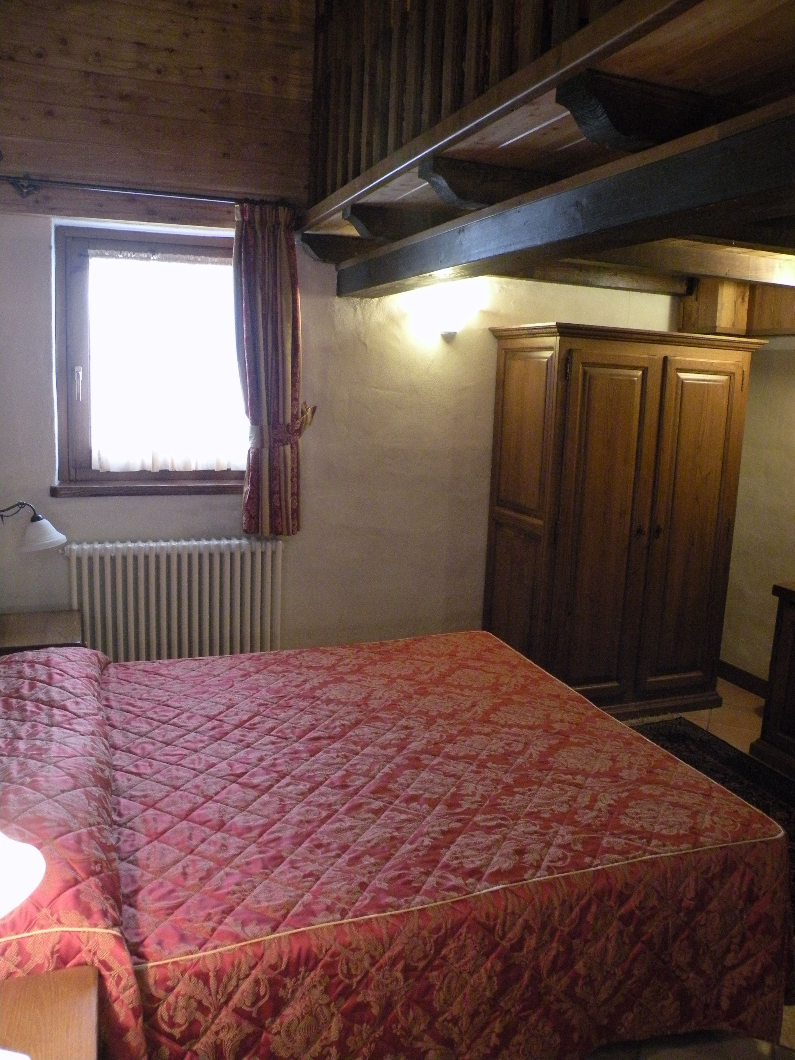 A bedroom with a bed, a window with curtains, a radiator, and wooden furniture.