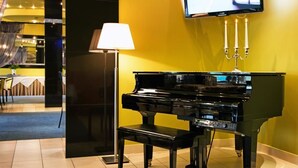 A black grand piano in a room with yellow walls, a lamp, and a television mounted on the wall. - Best Baltic Hotel Palanga (Palanga)