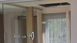 A modern bathroom with a glass shower enclosure, a wooden vanity, and a large window with a view of greenery. - Stössel's Hotel & Restaurant (Altenmedingen)