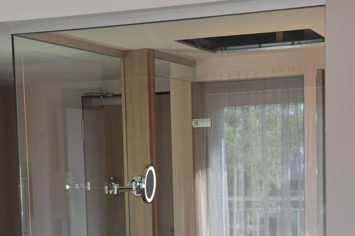 Un bagno moderno con box doccia in vetro, mobile lavabo in legno e un'ampia finestra vista verde.