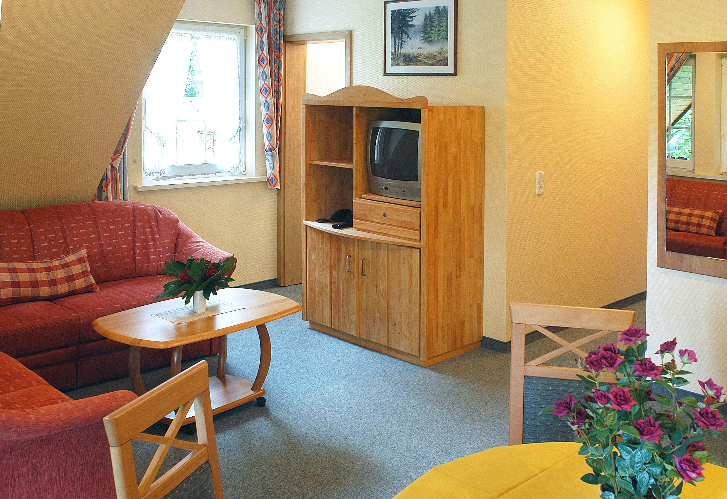 A cozy living room with a red sofa, a wooden entertainment unit with a television, and a small table with a vase of flowers.
