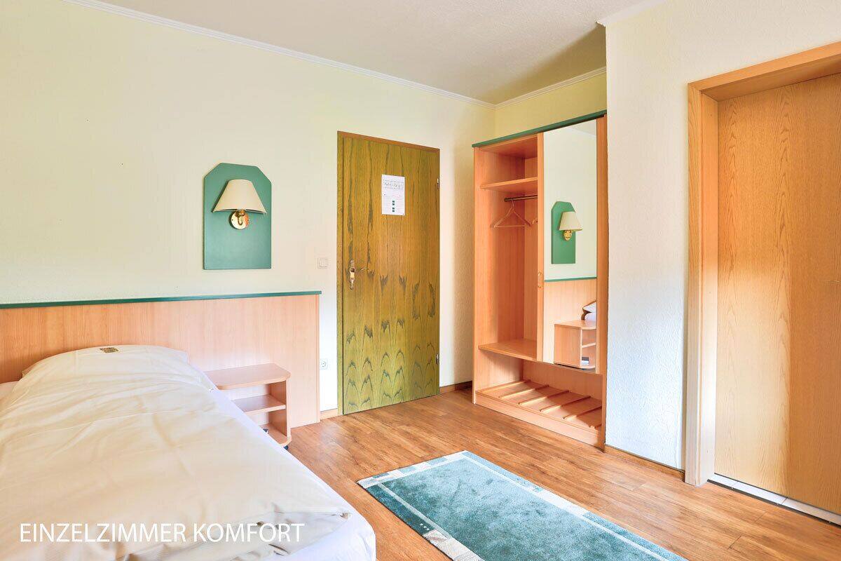 Una camera singola con un letto, un armadio in legno, uno specchio e una porta verde.