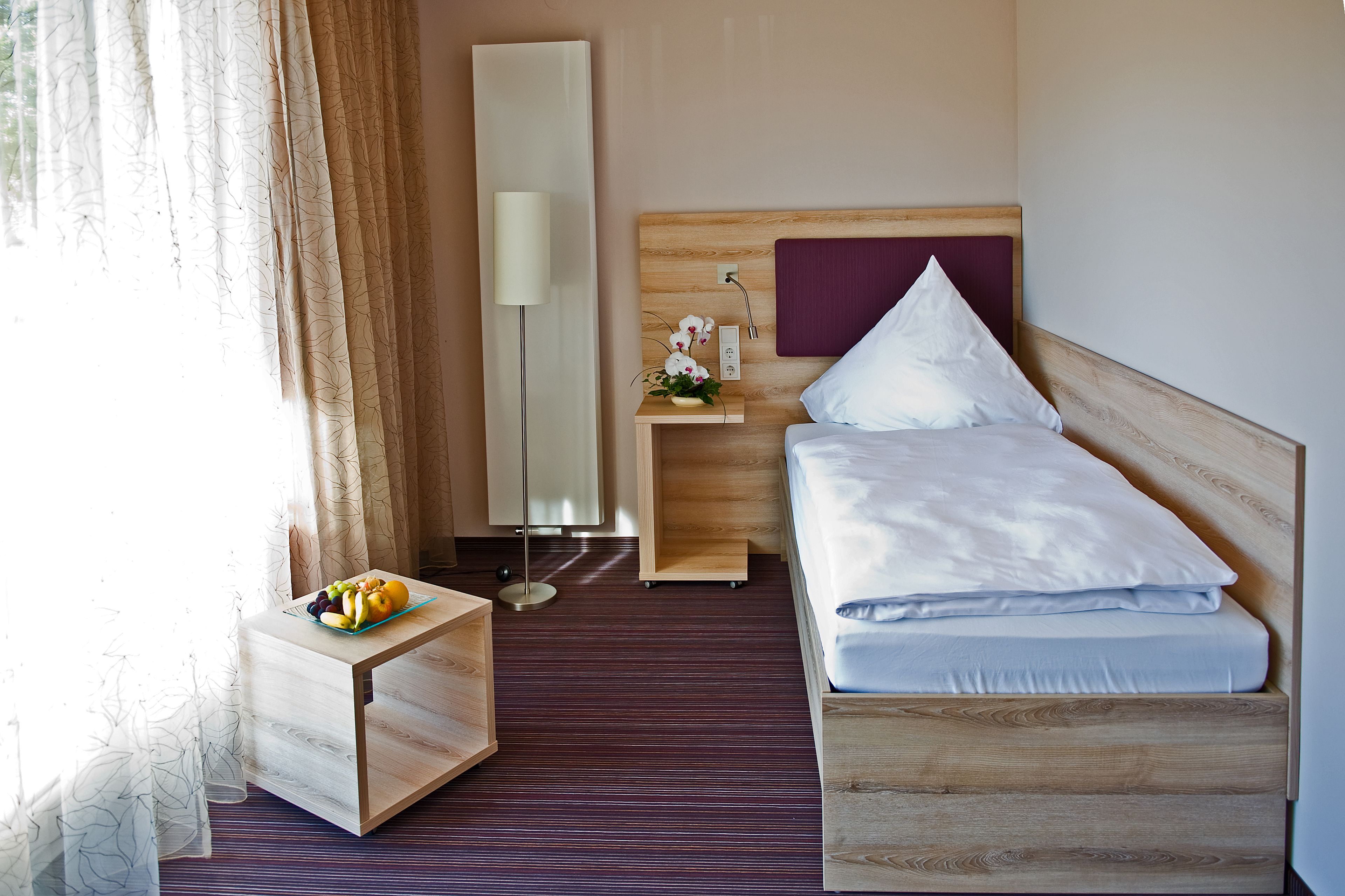 A hotel room with a wooden bed, a bedside table with a lamp, and a small table with fruit.
