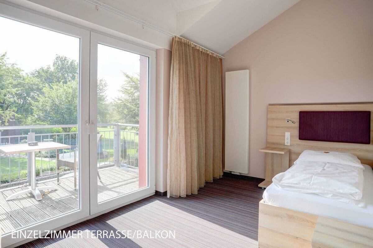 Una camera singola con balcone, un letto, un comodino e una testiera.