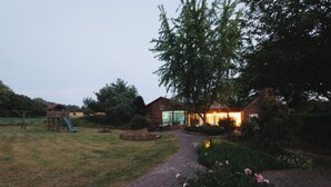 A residential property with a paved pathway, a wooden play structure, and a house with a lit interior. - Stössel's Hotel & Restaurant (Altenmedingen)