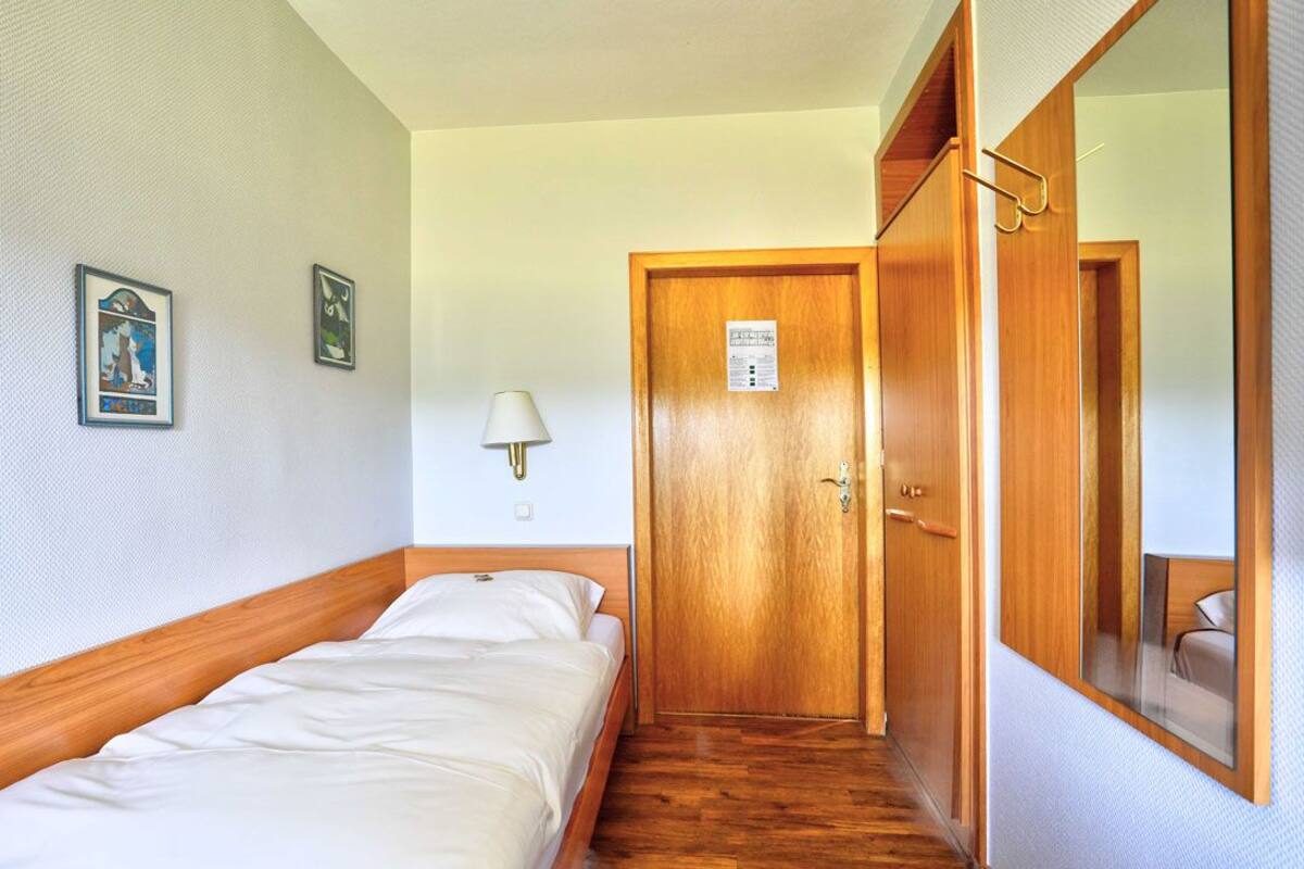 Una camera d'albergo con un letto singolo, un armadio in legno, uno specchio e due quadri appesi al muro.